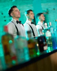 Tres bartenders con tirantes tras la barra en gala